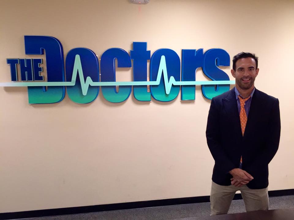 Jorge Cruise standing in front of The Doctors logo backstage at the studio